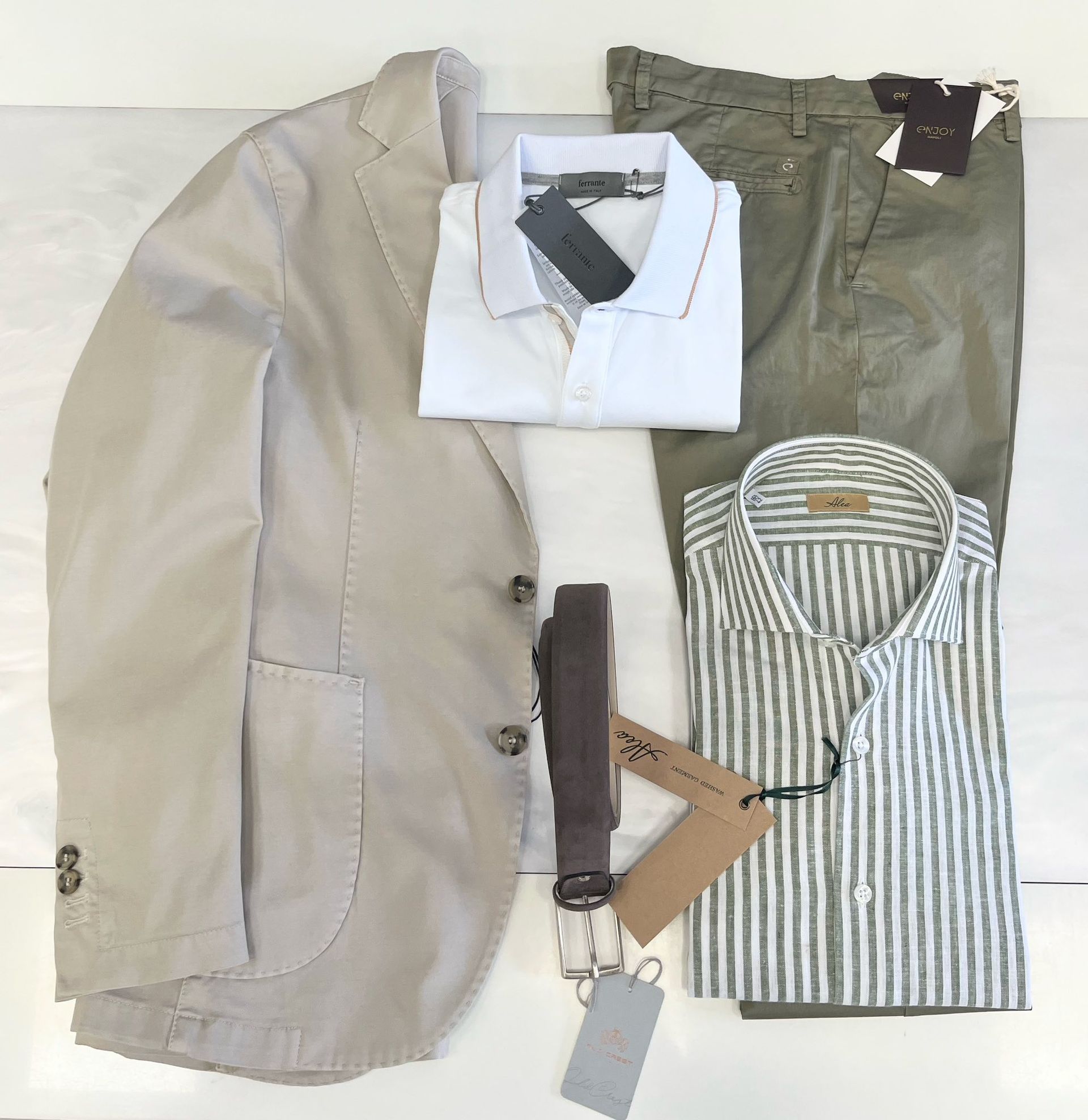 Vari capi di abbigliamento piegati, tra cui camicie, un blazer e accessori, disposti su una superficie bianca.