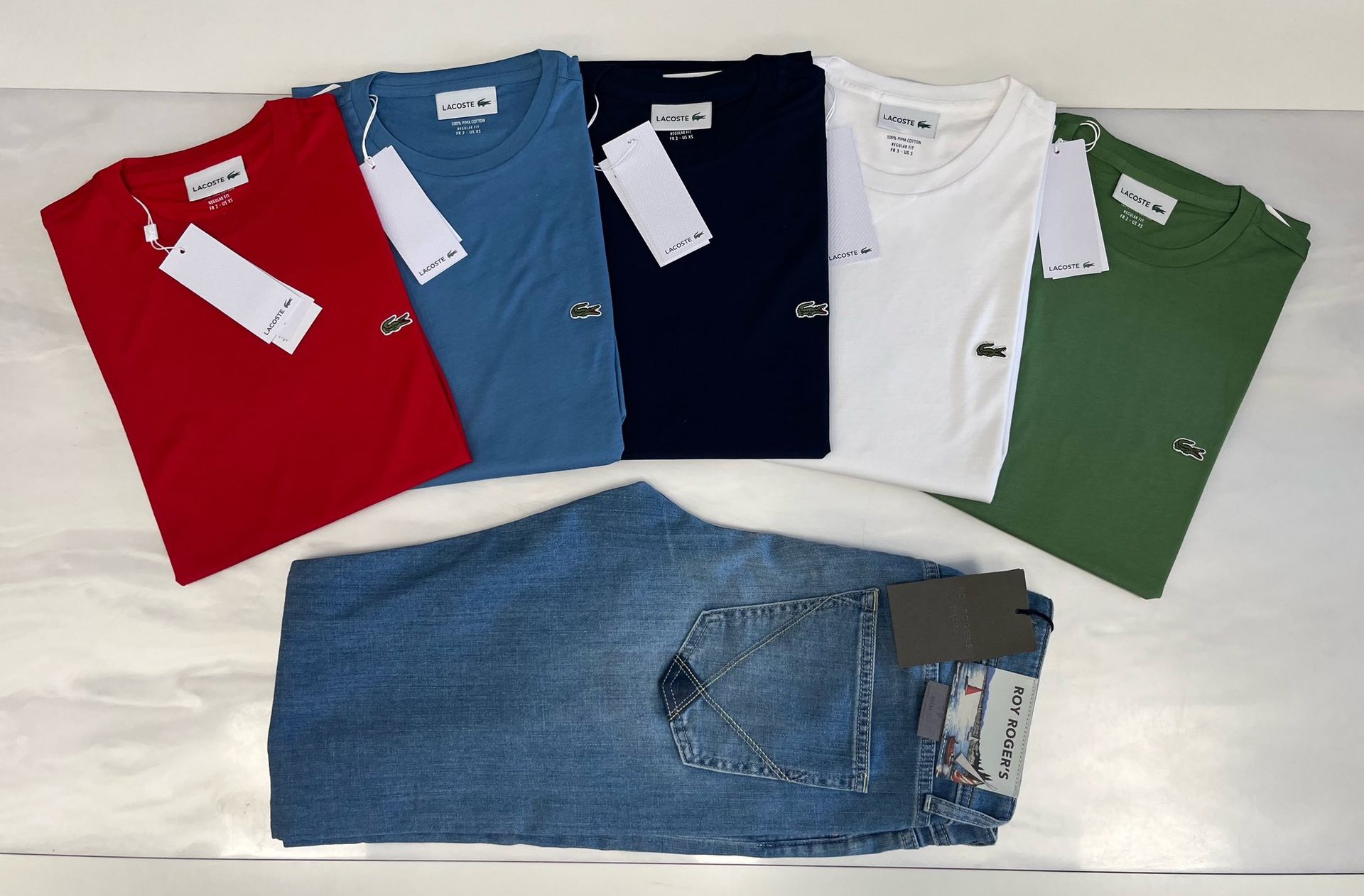 Magliette rosse, blu, blu scuro, bianche e verdi piegate sopra un paio di jeans blu piegati.
