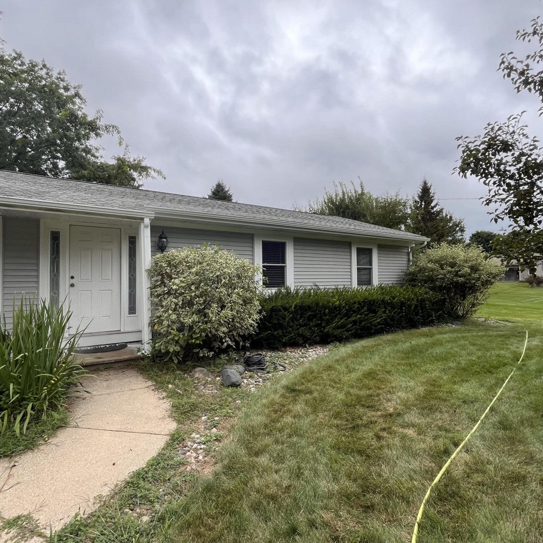 Light gray house with light green bushes, lawn, and cloudy sky.