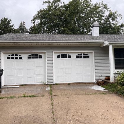 White garage doors on a gray house; concrete driveway in front.
