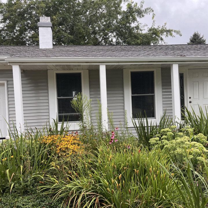 House with light gray siding, white columns and trim, and a lush garden in front.