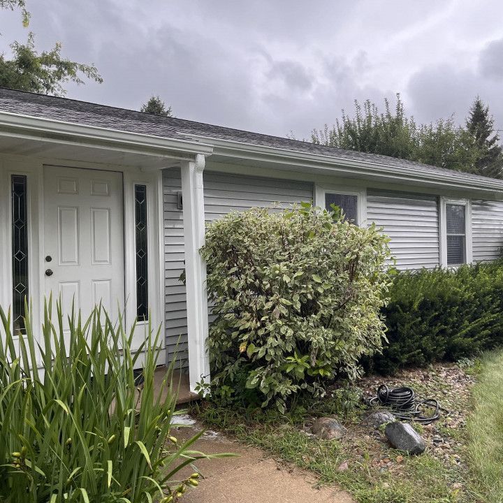Gray house with white door, bushes, and overcast sky.