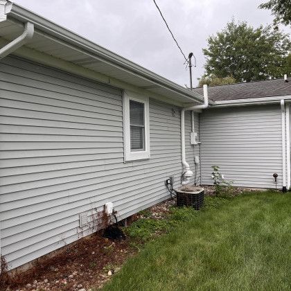 Gray siding on a house with a white window and gutters; green grass.