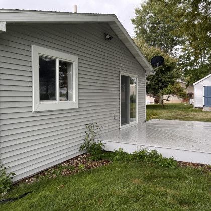 Gray house with white trim, window, and sliding glass door, a concrete patio, and green grass.