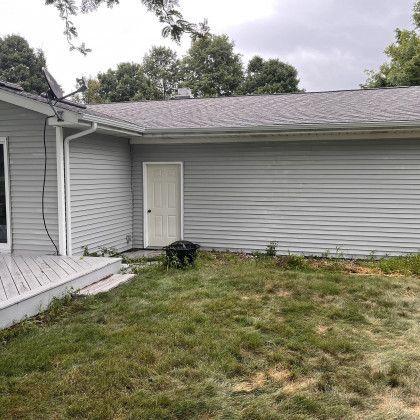 Gray house exterior with deck and yard, featuring a door, gray siding, and a fire pit.