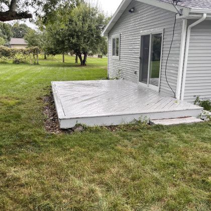 Grey deck next to a house with a sliding door, overlooking a grassy yard.