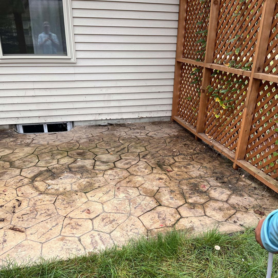 Concrete patio with a patterned surface next to a wooden lattice and a window on a siding wall.