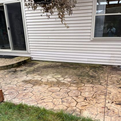 Honeycomb patterned concrete patio next to a house with a sliding glass door and white siding.