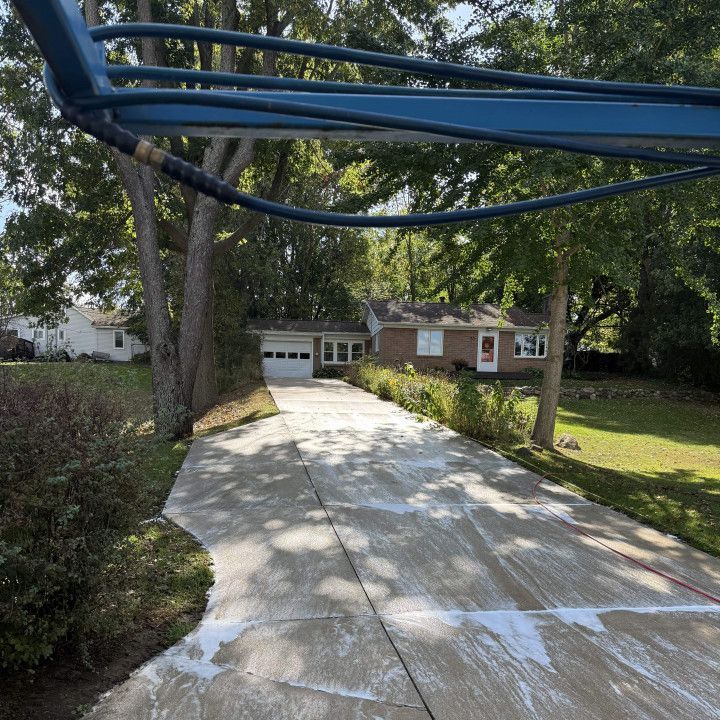 Driveway being power washed; house in background with trees overhead.