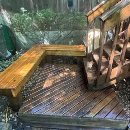 Wooden deck with bench and stairs, freshly treated, set against a wooden wall and foliage.