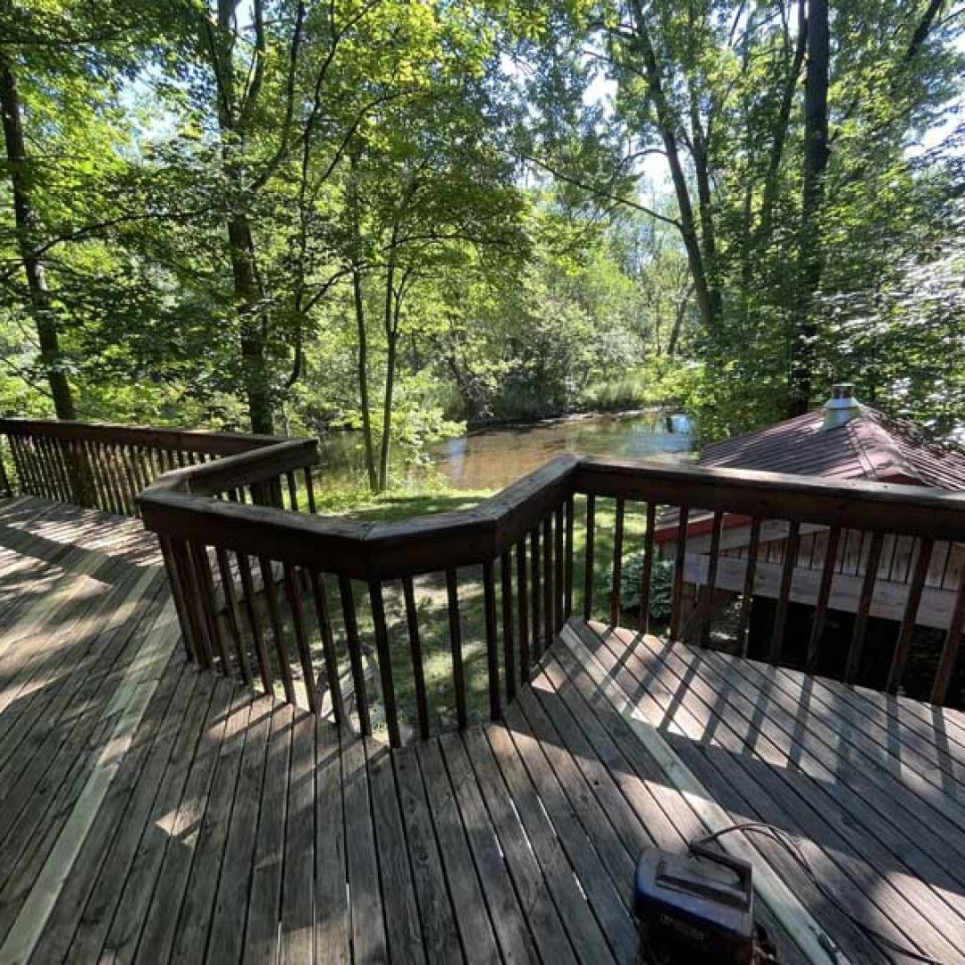 Wooden deck overlooking a river, with a gazebo and trees in the background. Sunny day.