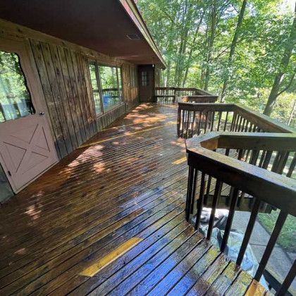 Wooden deck with railing alongside a cabin, surrounded by trees.