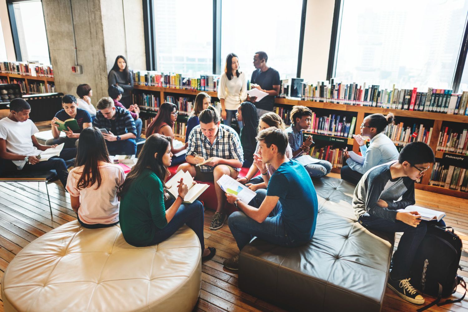 Students sitting in a library, reading and talking in small groups around tables