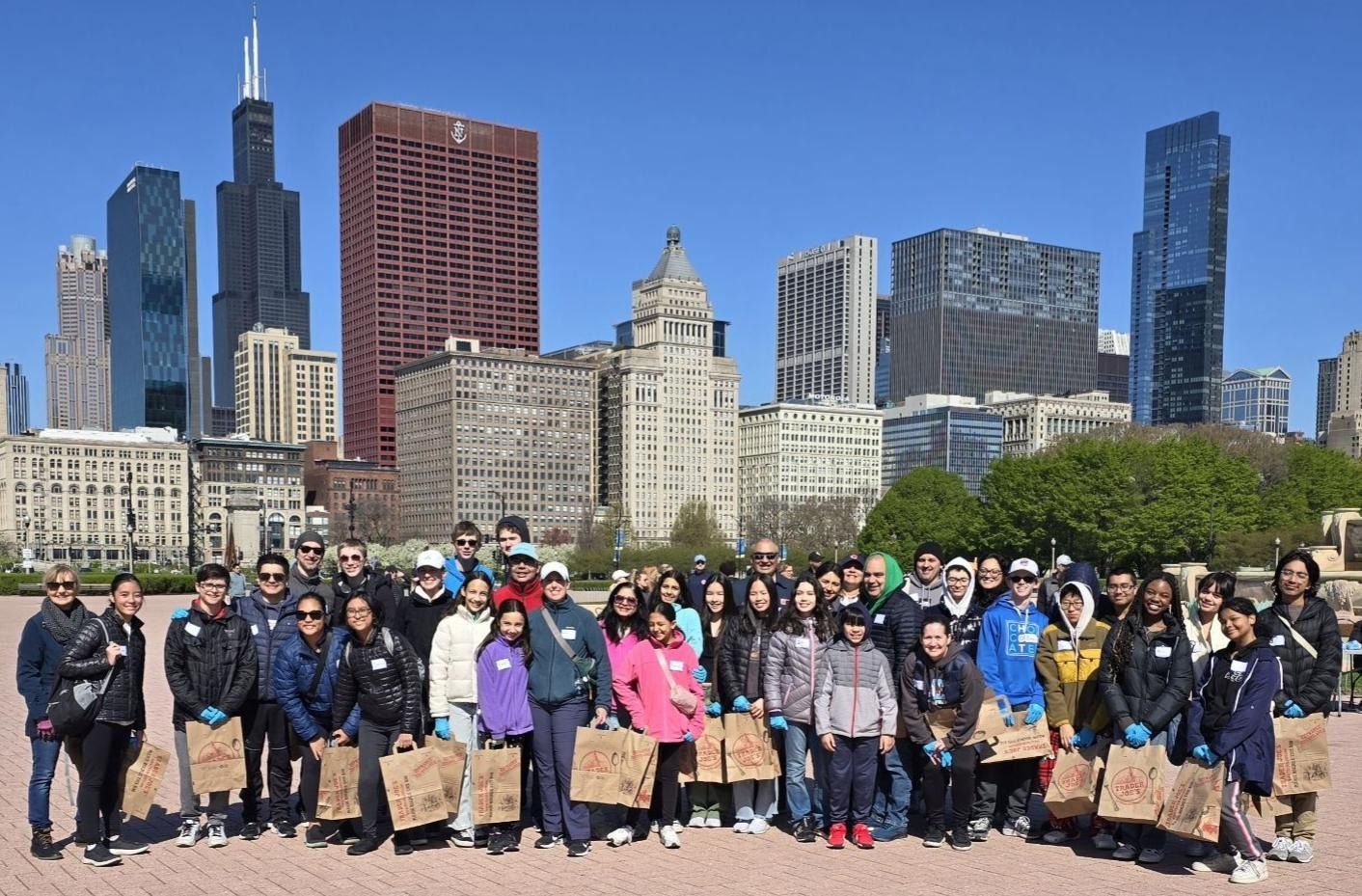 Large group posing outdoors with downtown Chicago skyline behind them on a sunny day