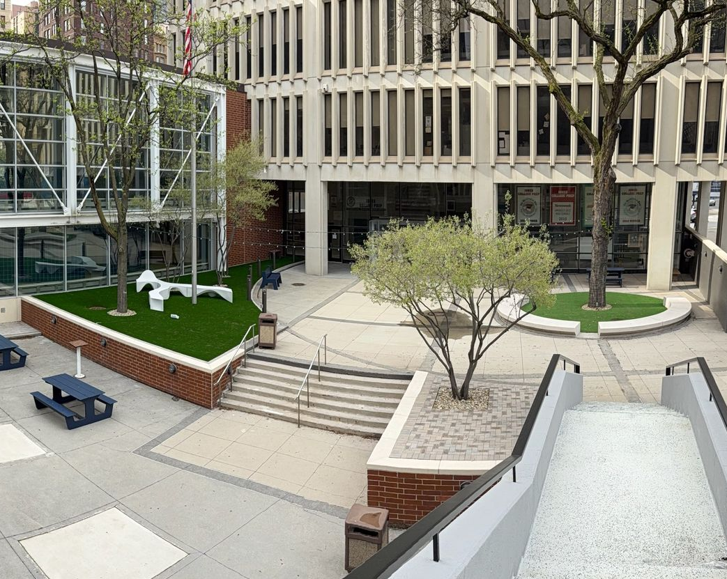 Modern courtyard with steps, a small tree, benches, and a glass-and-stone building facade