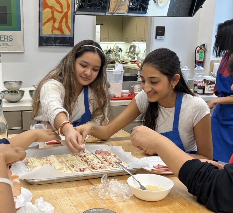 People sharing and serving pizza dough at a kitchen table, smiling in a cooking class