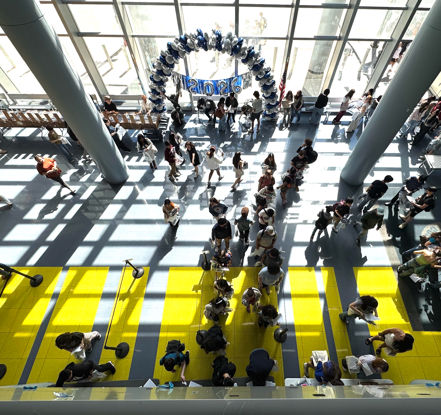 Crowded indoor atrium with people walking below a blue circular art display and bright yellow floor panels