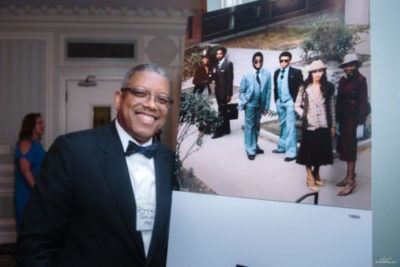 Man smiling beside a large wedding photo display at an indoor event