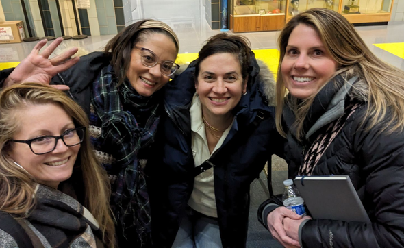 Four smiling friends pose for a selfie outdoors, wearing winter coats and scarves.