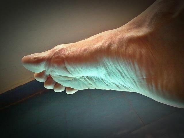 Close-up of a bare foot, lit with a warm glow, resting on a dark surface.