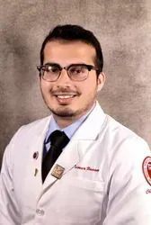 Man in white coat, smiling, in a medical setting.