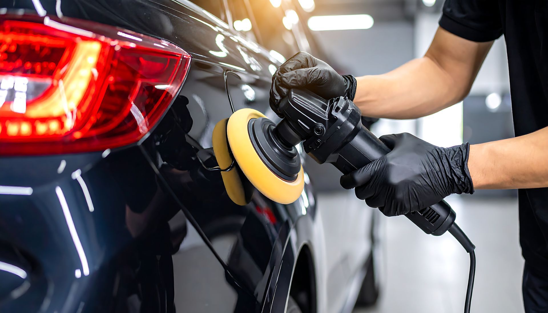 Person polishing a black car with a yellow buffer in a garage | 
Valued Auto Care LLC