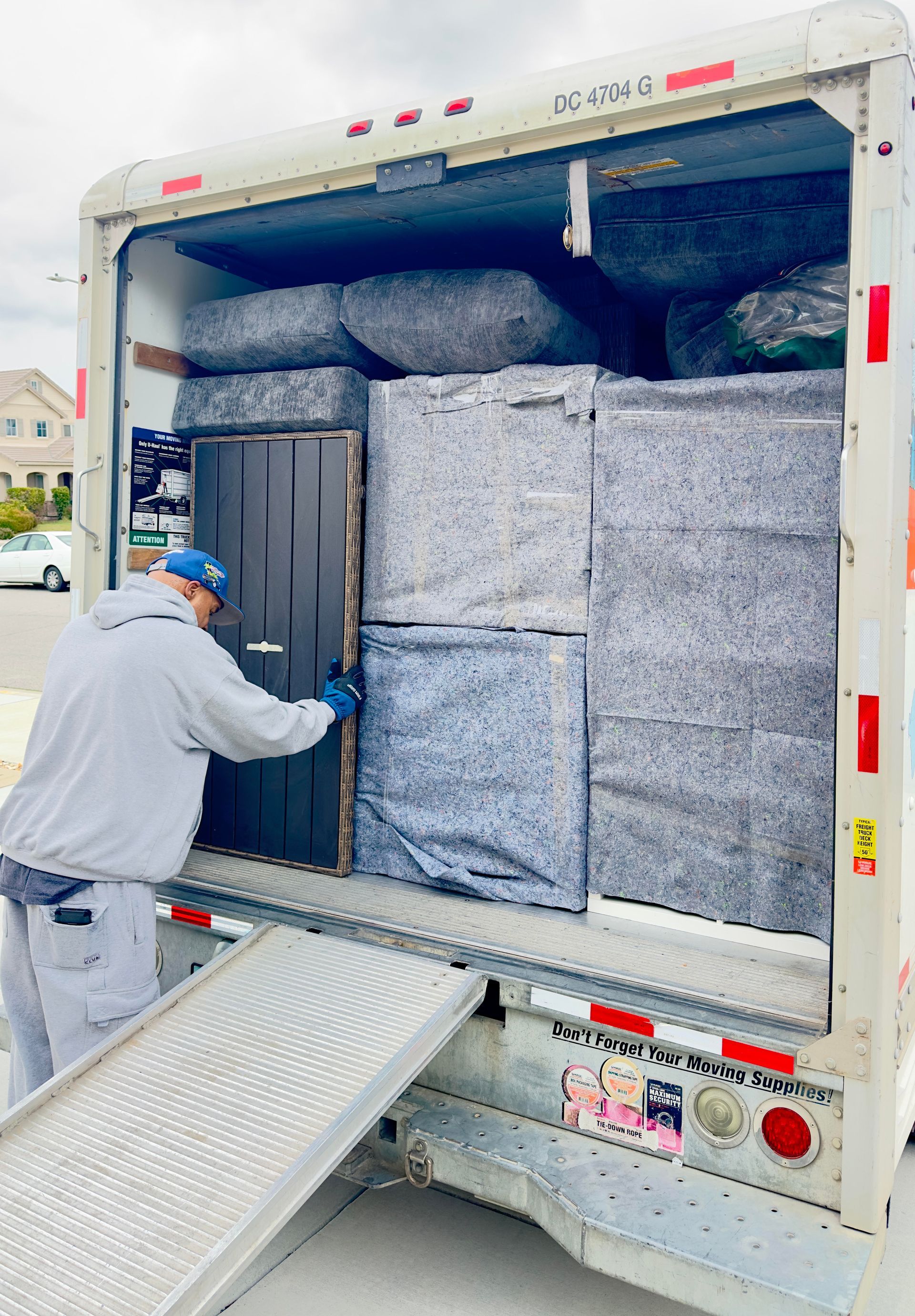 Man loads truck bed packed with wrapped furniture and boxes. Ramp extended.