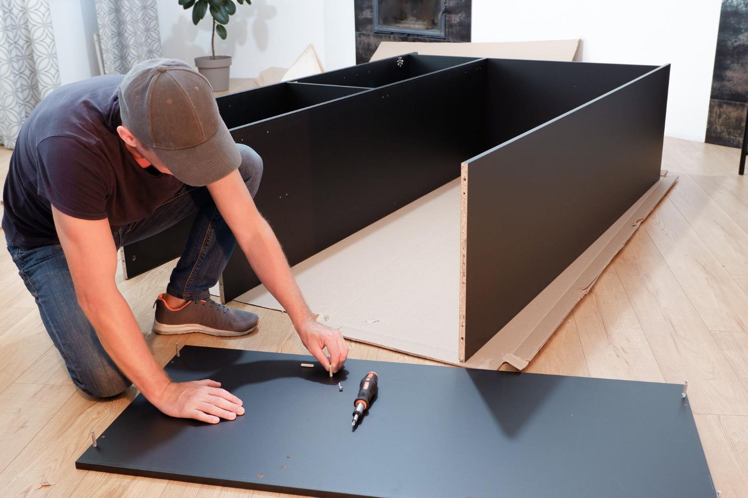 Man assembling a black cabinet on a wood floor.