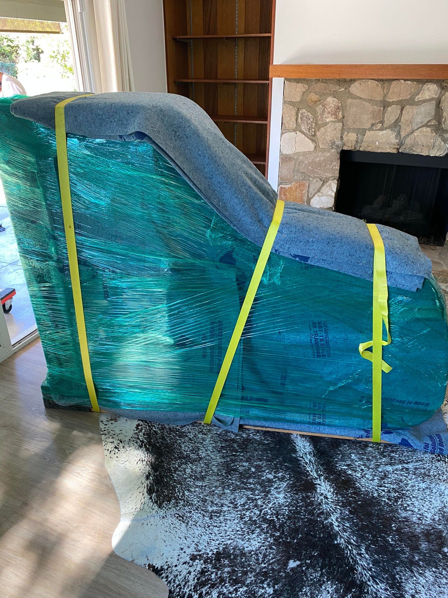 A piano is wrapped in plastic and sitting on a rug in a living room.
