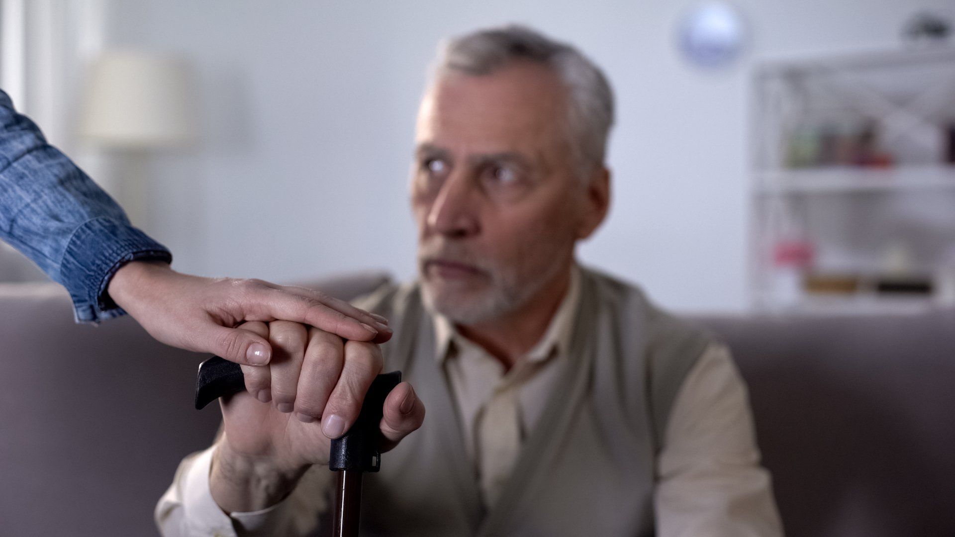 A woman is holding the hand of an elderly man with a cane.
