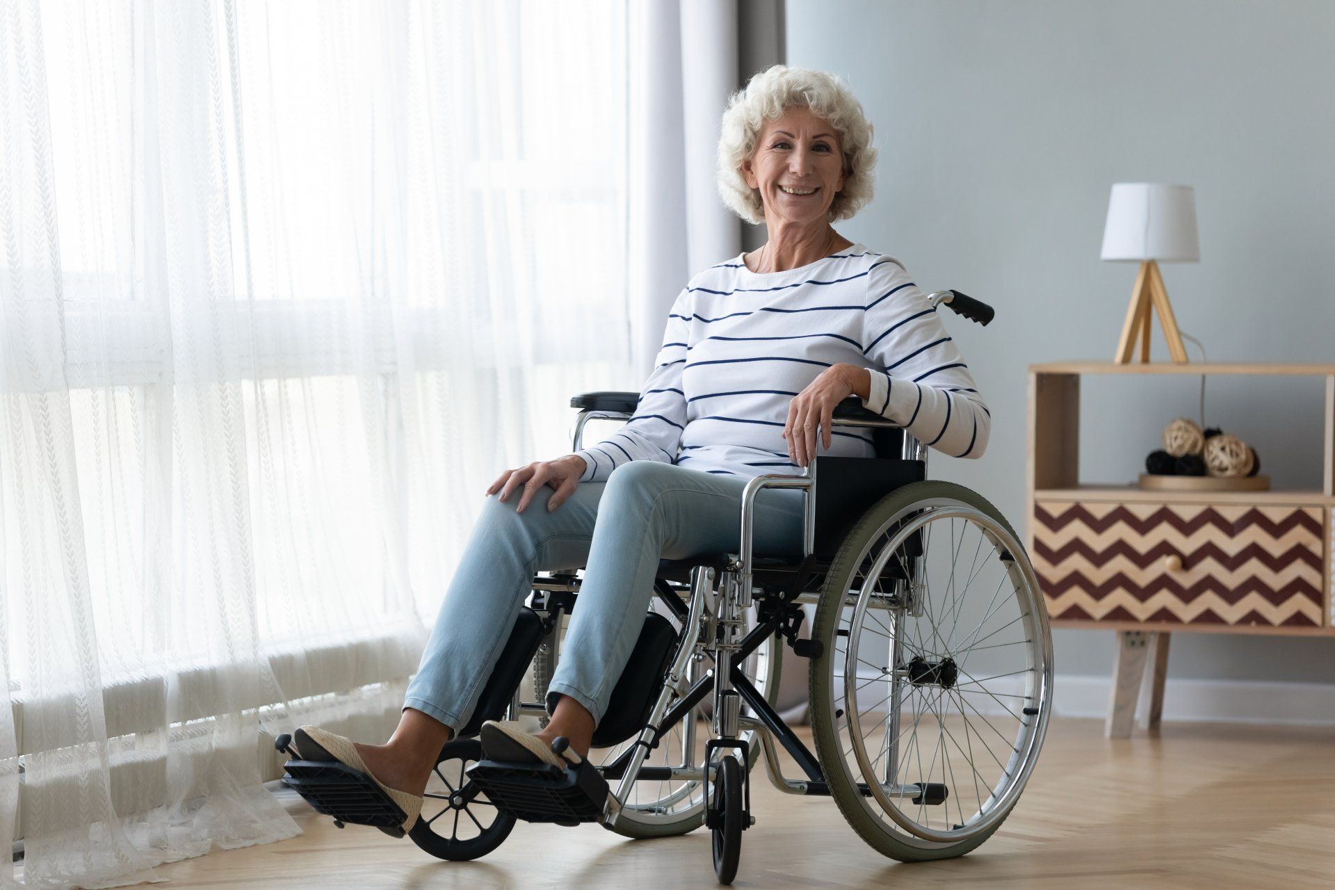 An elderly woman is sitting in a wheelchair in front of a window.