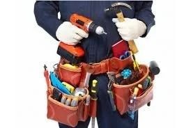 Person wearing a tool belt holding a drill and hammer on a construction site