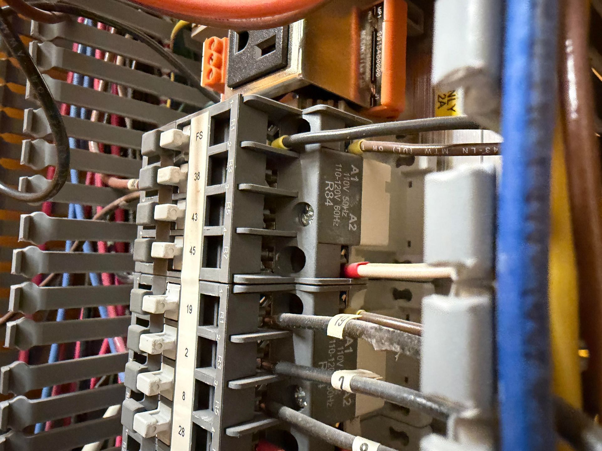 Gloved hands using a digital multimeter to test wiring inside an electrical panel
