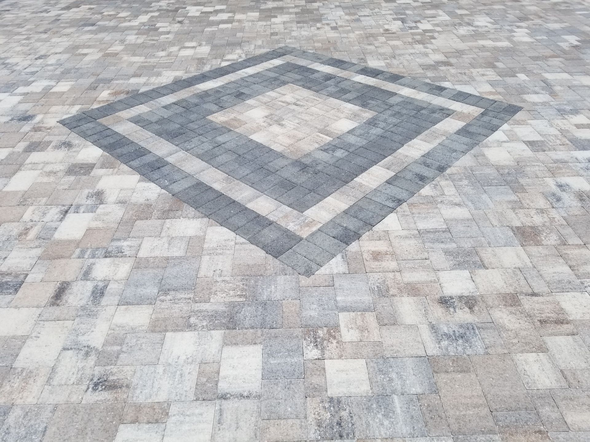 A paved surface with a large, dark gray diamond pattern centered within a light gray and beige stone tile background.