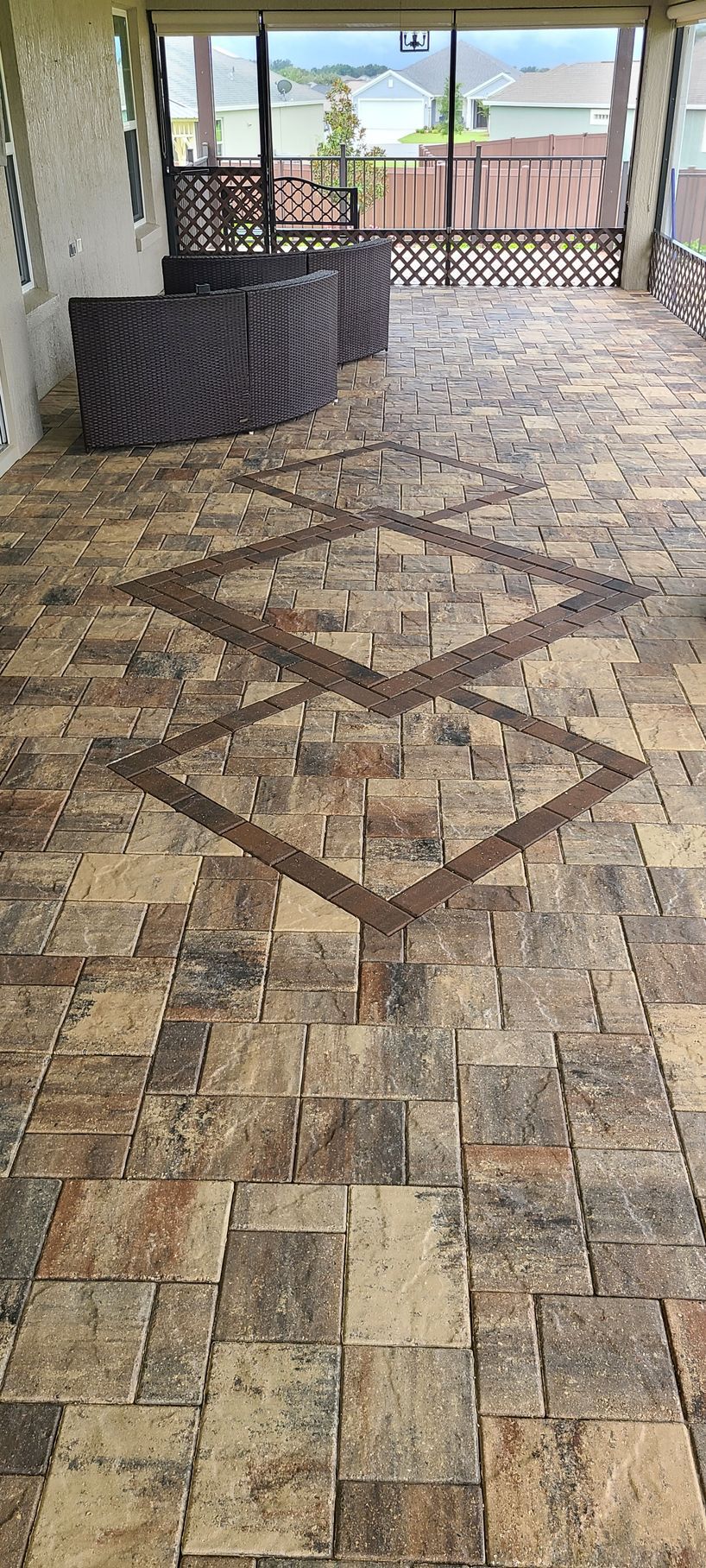 A covered patio with tan and brown stone pavers featuring a decorative diamond-shaped pattern inlaid in the floor.