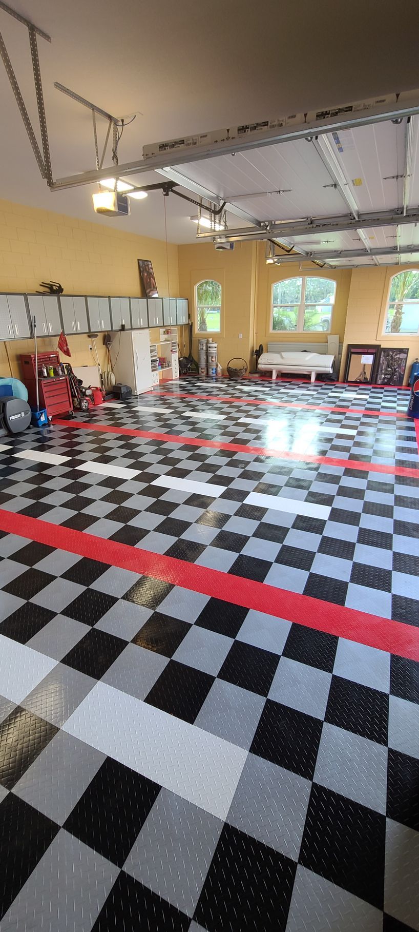 A garage with a black, grey, and white checkered floor, featuring red accent stripes and built-in storage cabinets.