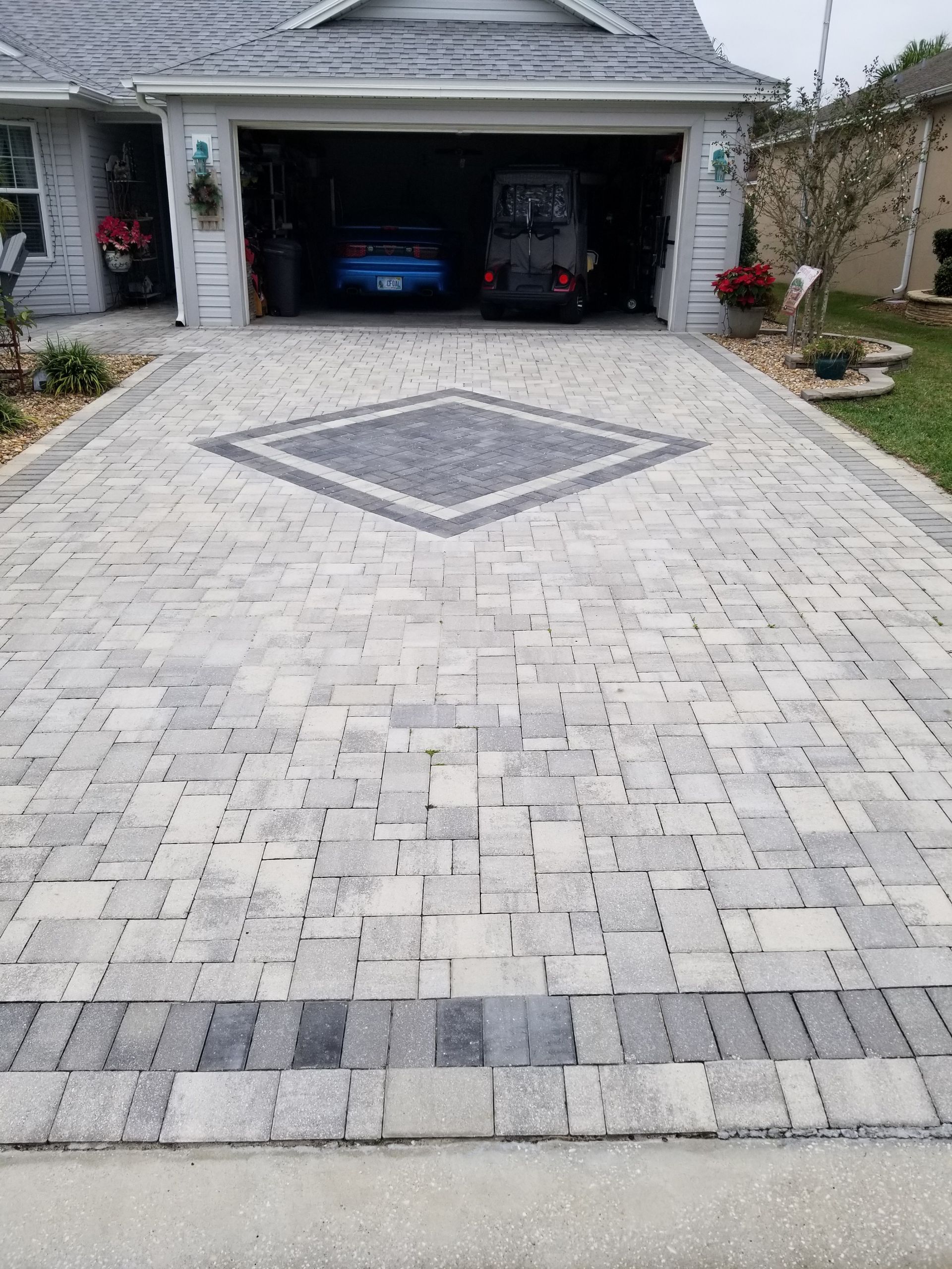 A gray paver driveway with a central diamond-shaped dark gray accent inlay leading to a residential garage.