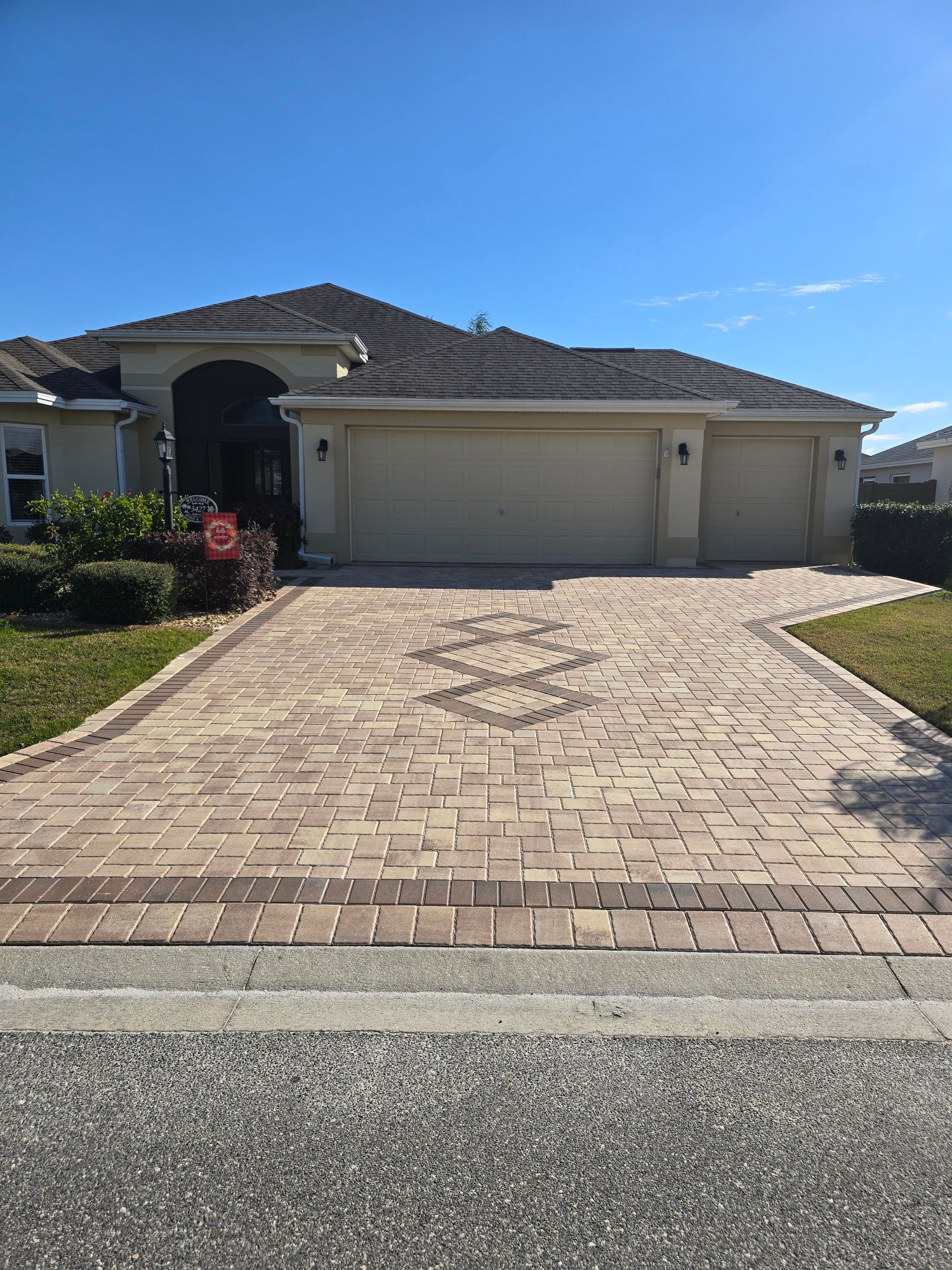 A suburban home exterior featuring a paver driveway with a decorative pattern, leading to a multi-car garage.