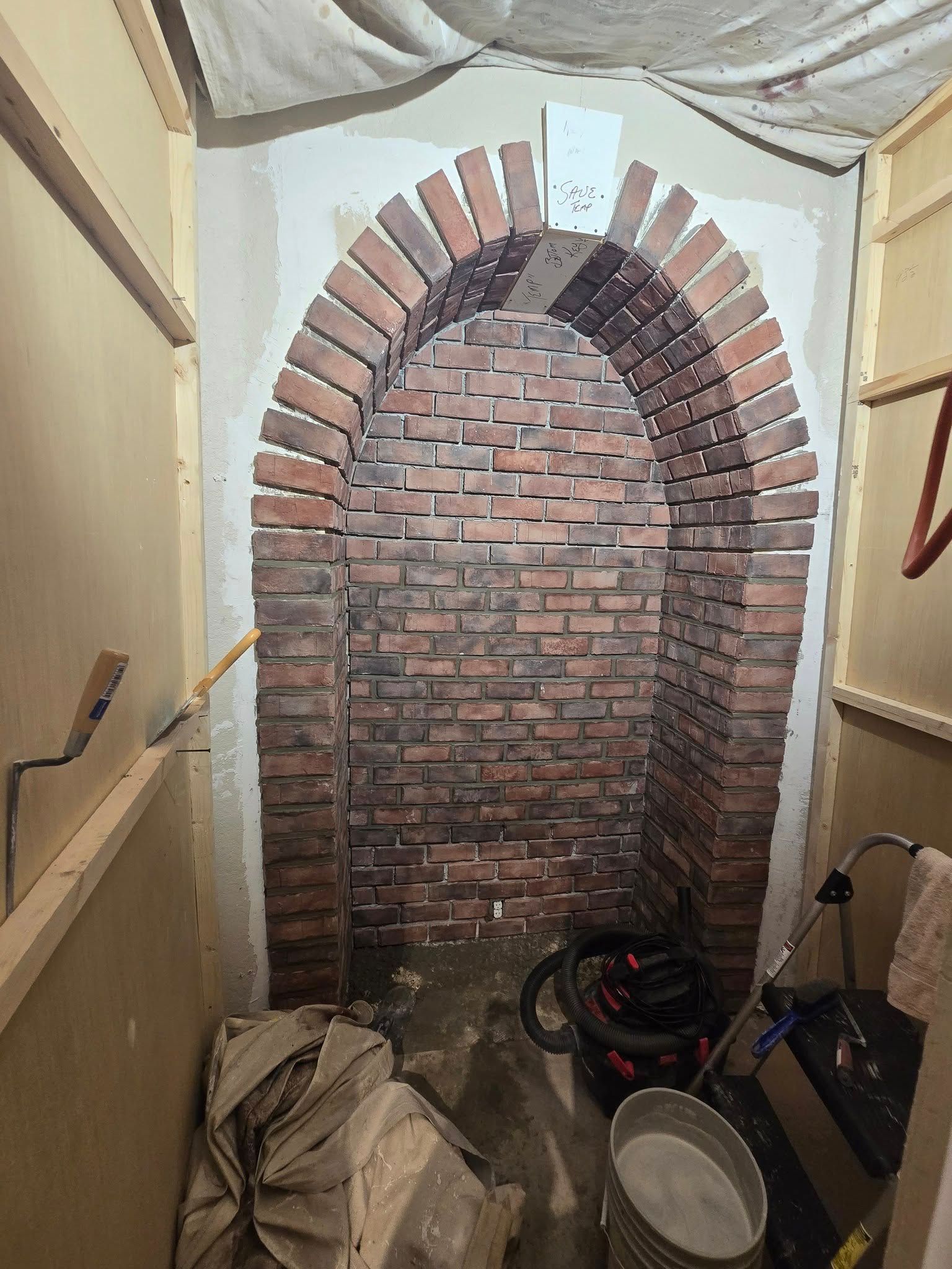 A brick-lined arched alcove set into a wall under construction with tools and supplies on the floor.