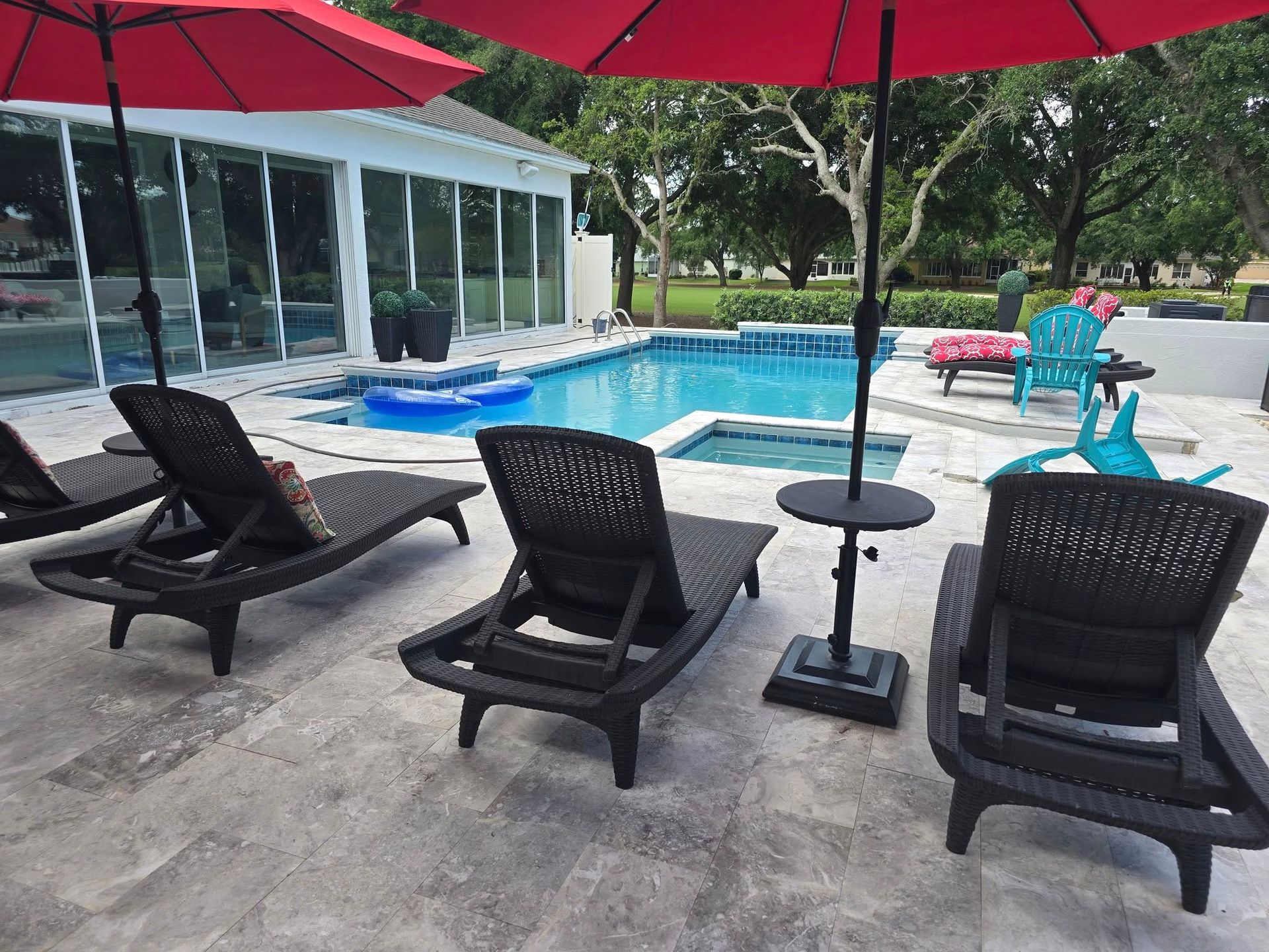 Black lounge chairs and red umbrellas on a stone patio overlooking a rectangular swimming pool and hot tub.