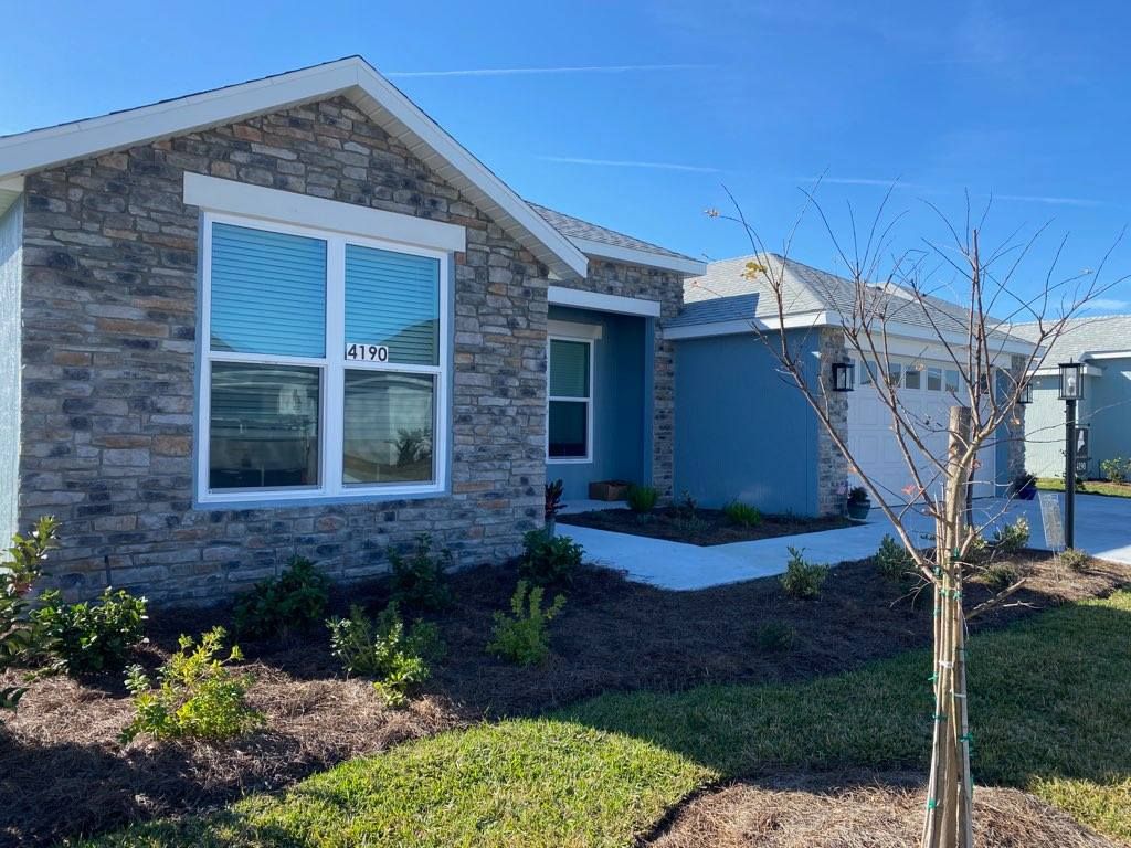 A single-story suburban house with stone veneer siding, a blue painted section, a garage, and a landscaped front yard.