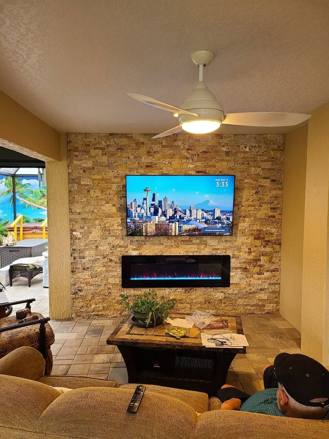 A stone fireplace wall with a mounted flat-screen TV and electric fireplace insert, viewed from a cozy indoor patio area.