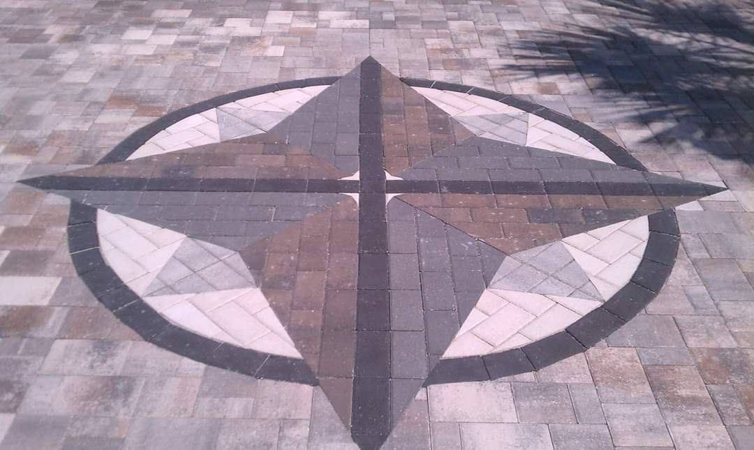 A stone paver medallion on a patio featuring a star design in shades of gray and tan inside a dark circular border.