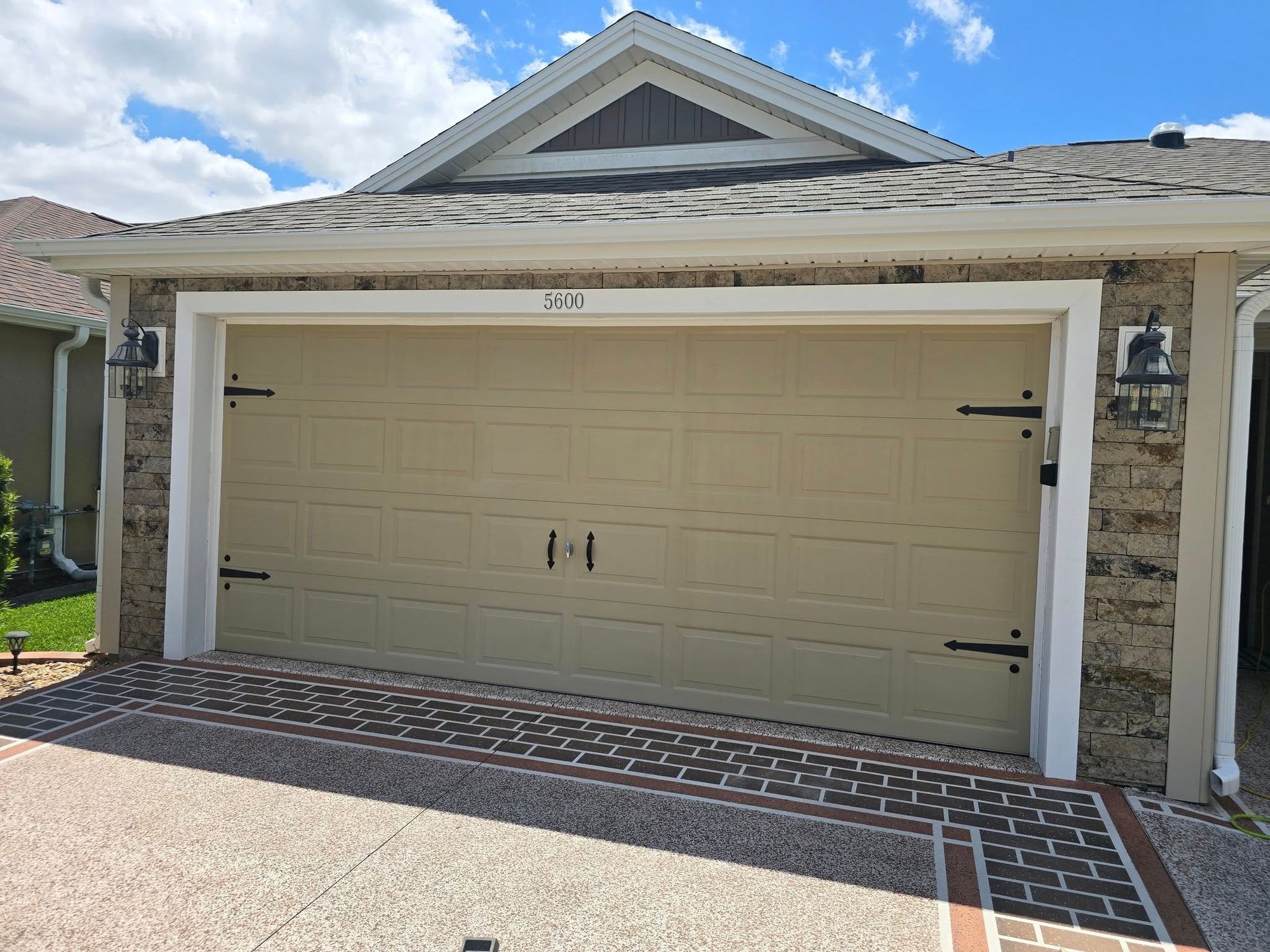 A beige, single-car garage door with decorative black hinges, set in a house with a stone-textured exterior.