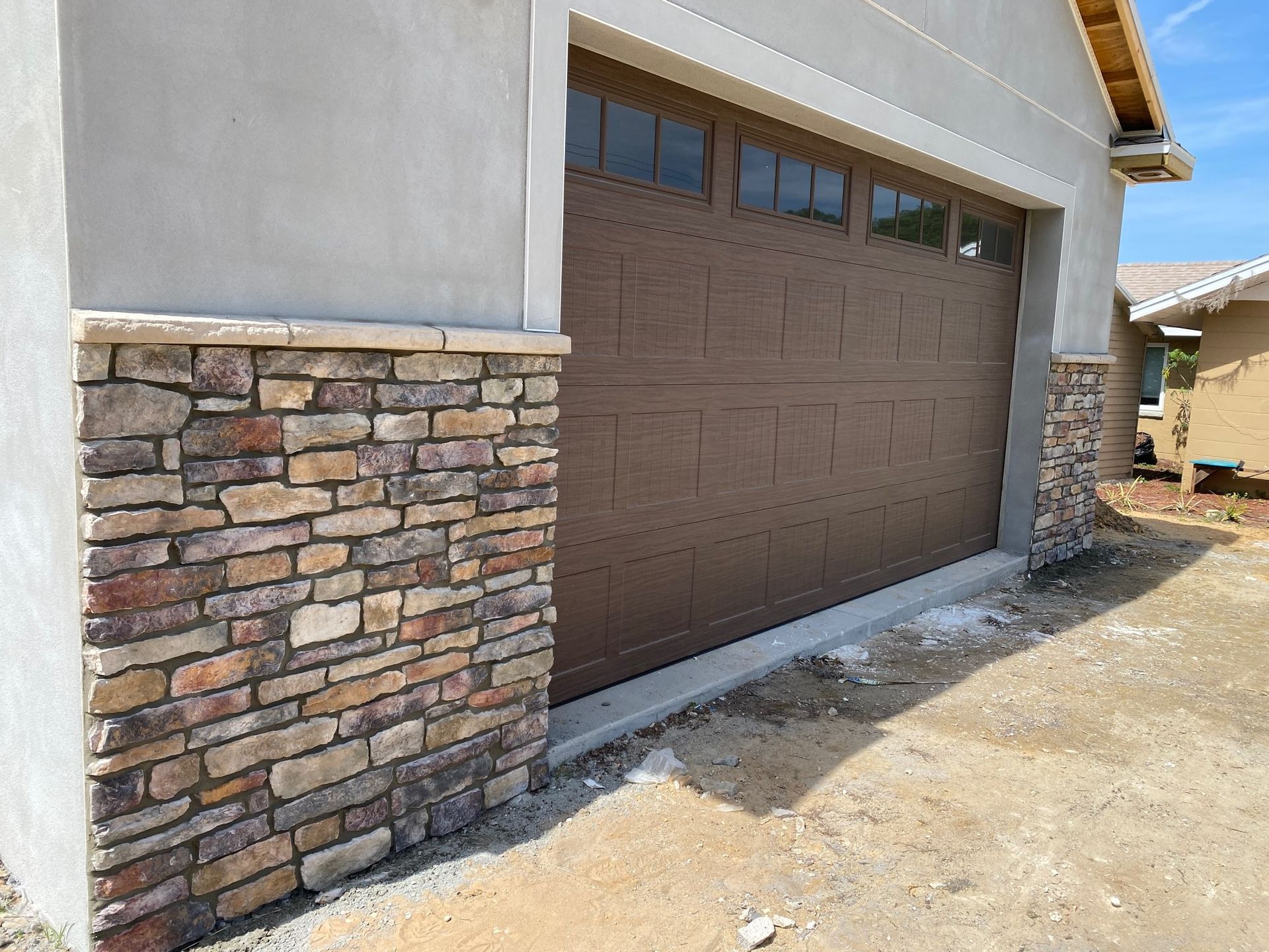 A residential garage featuring brown doors with windows, surrounded by decorative stone veneer and light-colored stucco.