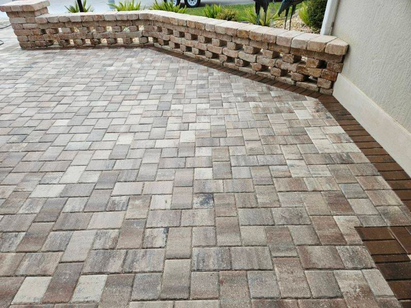 A patio with multicolored, rectangular pavers arranged in a brick pattern beside a low, open-patterned brick garden wall.