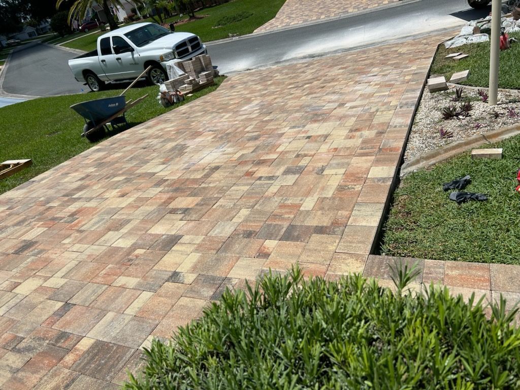 A newly installed paved driveway made of multi-colored rectangular stone blocks leads toward a white pickup truck.