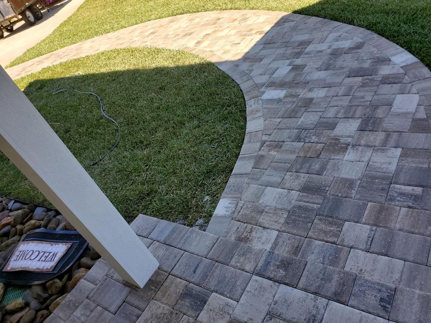A curved walkway made of grey and brown rectangular pavers leading from a lawn toward a building's entrance.