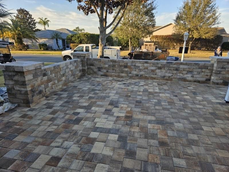 A paved stone patio with a matching low stone wall in a sunny residential yard.