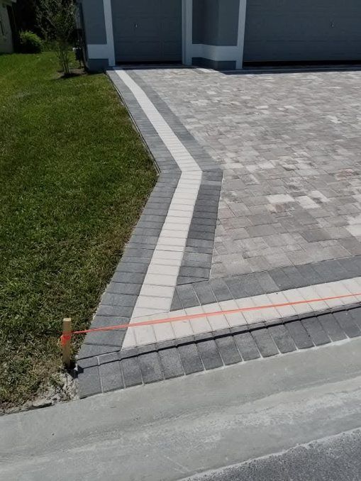 A paved driveway featuring a light gray border and dark gray accents leading to a garage, with a grass lawn to the side.